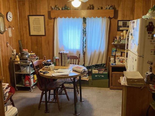 dining space with carpet, ceiling fan, and wooden walls