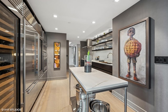 kitchen featuring a kitchen island, sink, light hardwood / wood-style flooring, appliances with stainless steel finishes, and wall chimney exhaust hood