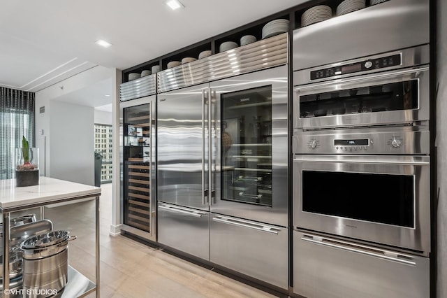 kitchen with stainless steel double oven, light hardwood / wood-style flooring, and wine cooler