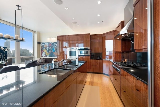 kitchen with decorative light fixtures, wall chimney range hood, sink, light wood-type flooring, and appliances with stainless steel finishes