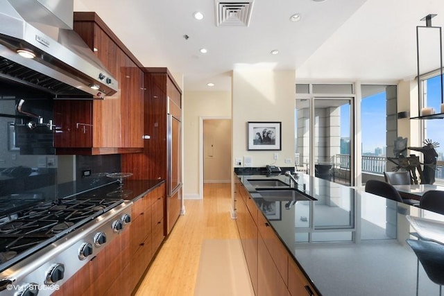 kitchen featuring light hardwood / wood-style floors, extractor fan, backsplash, stainless steel gas cooktop, and hanging light fixtures