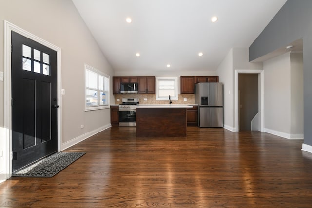 kitchen with a kitchen island, stainless steel appliances, backsplash, dark hardwood / wood-style floors, and vaulted ceiling