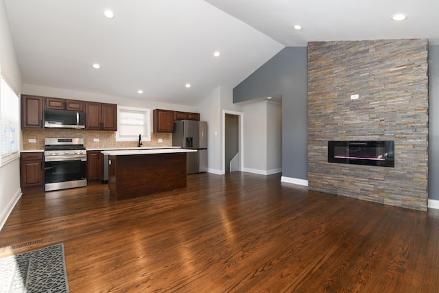 kitchen featuring appliances with stainless steel finishes, a kitchen island, a stone fireplace, decorative backsplash, and dark hardwood / wood-style floors