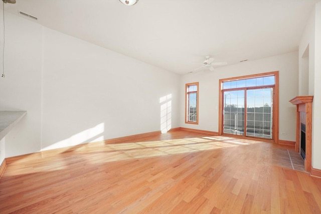 unfurnished living room with light wood-type flooring, ceiling fan, and a tiled fireplace