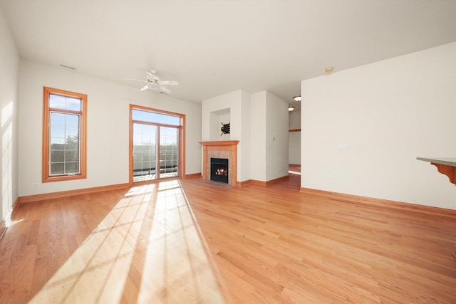 unfurnished living room with ceiling fan, a tile fireplace, and light hardwood / wood-style flooring