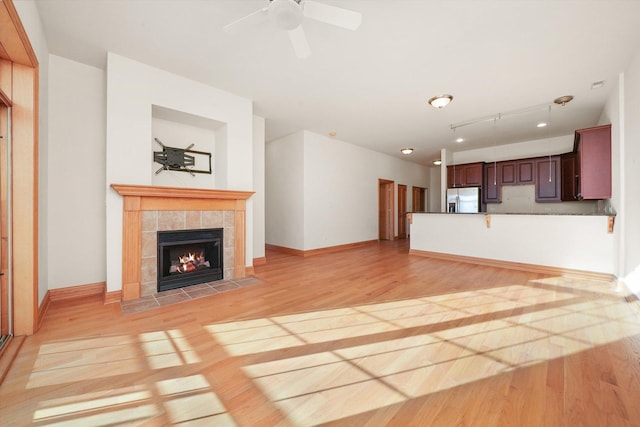 unfurnished living room with ceiling fan, a tile fireplace, and light hardwood / wood-style flooring