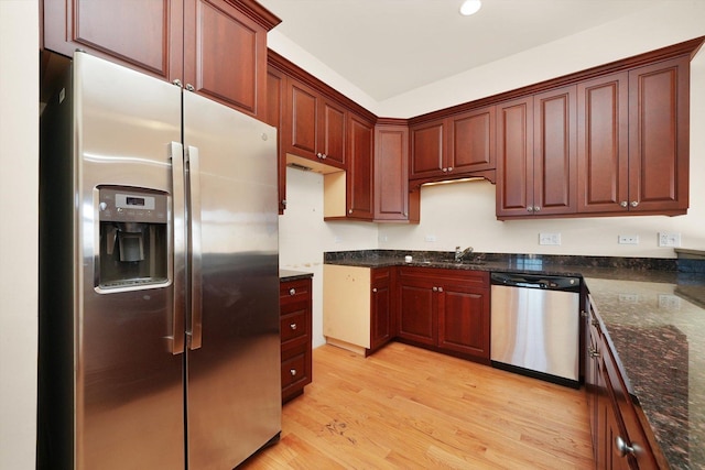 kitchen featuring light wood-type flooring, stainless steel appliances, dark stone counters, and sink