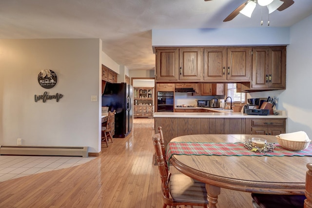 kitchen featuring sink, light wood-type flooring, a baseboard heating unit, kitchen peninsula, and black appliances