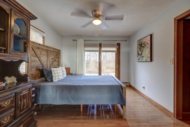 bedroom featuring baseboard heating, ceiling fan, light hardwood / wood-style floors, and a textured ceiling