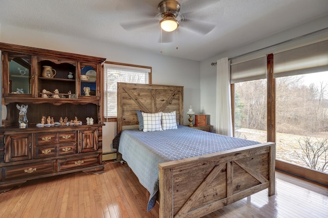 bedroom featuring multiple windows, access to exterior, baseboard heating, and light wood-type flooring