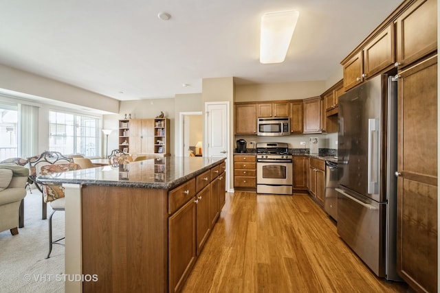 kitchen featuring appliances with stainless steel finishes, a kitchen breakfast bar, a kitchen island, dark stone counters, and light hardwood / wood-style floors