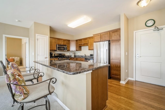 kitchen featuring appliances with stainless steel finishes, a breakfast bar, dark stone countertops, a center island, and light hardwood / wood-style flooring