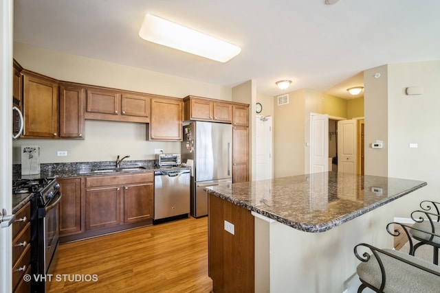 kitchen featuring a breakfast bar, sink, dark stone countertops, stainless steel appliances, and light hardwood / wood-style flooring