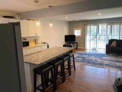 kitchen featuring stainless steel fridge, a kitchen breakfast bar, hanging light fixtures, light stone countertops, and white cabinets