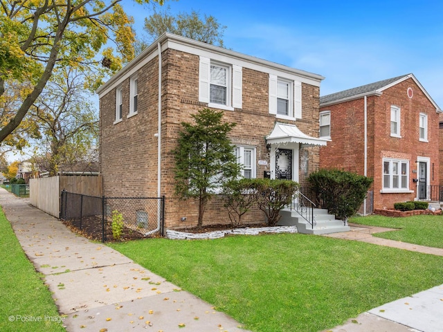 view of front facade with brick siding, a front yard, and fence