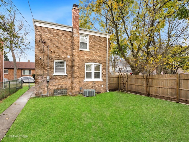 back of property with brick siding, a fenced backyard, a chimney, and a yard