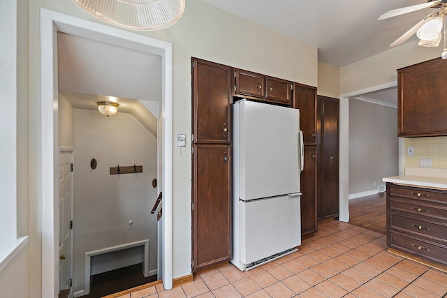 kitchen featuring dark brown cabinetry, light tile patterned floors, ceiling fan, and white fridge