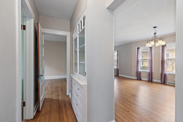 hall with an inviting chandelier, a baseboard radiator, and wood-type flooring