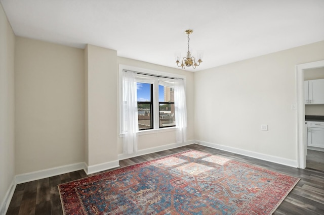 empty room with a notable chandelier and dark hardwood / wood-style floors