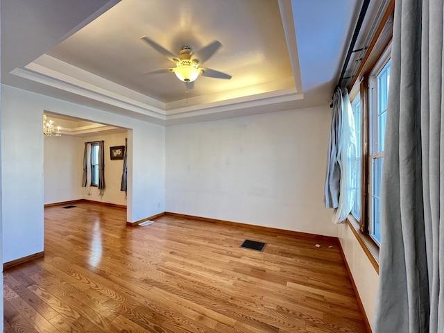 unfurnished room featuring ceiling fan with notable chandelier, light hardwood / wood-style flooring, and a raised ceiling