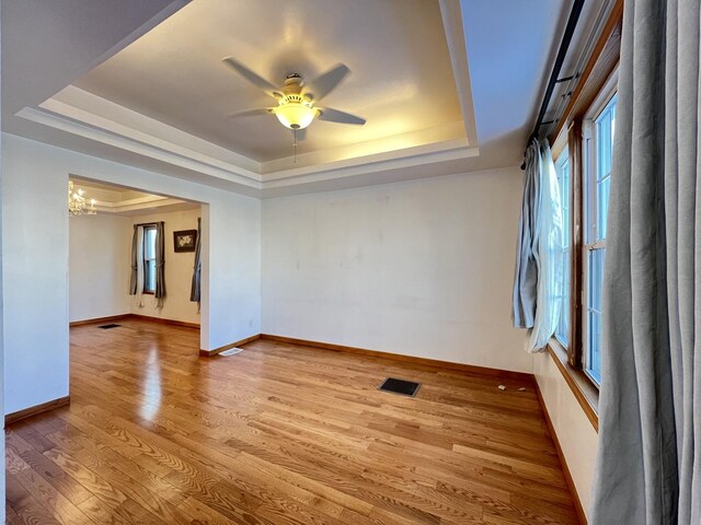 spare room featuring ceiling fan with notable chandelier, light hardwood / wood-style floors, and a tray ceiling