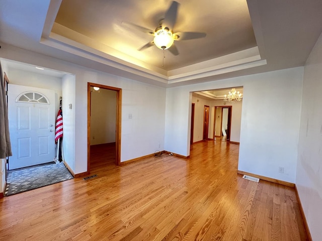 spare room featuring a raised ceiling, ceiling fan with notable chandelier, and light hardwood / wood-style flooring