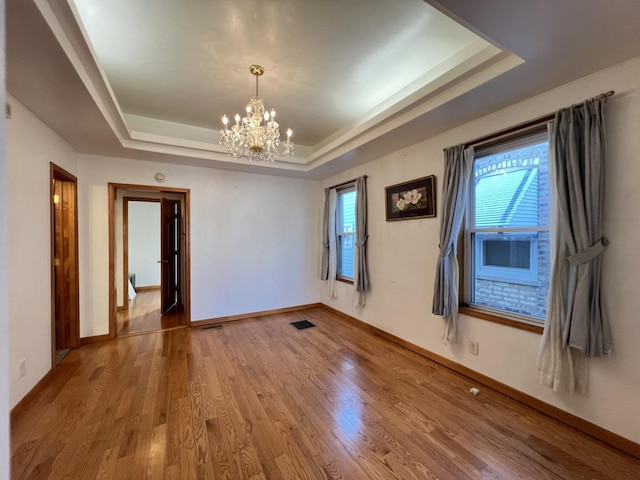 empty room featuring an inviting chandelier, wood-type flooring, a raised ceiling, and a healthy amount of sunlight