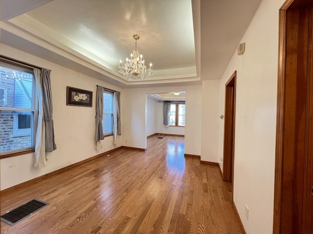 unfurnished room featuring an inviting chandelier, light hardwood / wood-style floors, and a raised ceiling