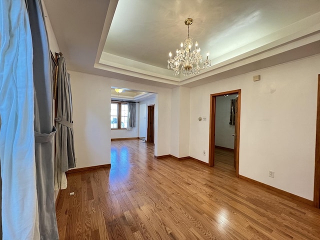 unfurnished dining area featuring an inviting chandelier, wood-type flooring, and a raised ceiling