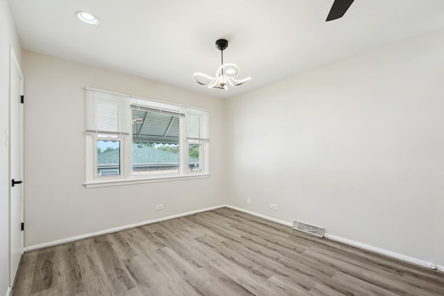 spare room with ceiling fan with notable chandelier and light hardwood / wood-style flooring