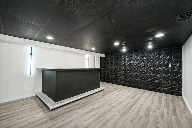 interior space featuring light wood-type flooring, a drop ceiling, and bar