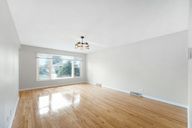 empty room featuring an inviting chandelier and light hardwood / wood-style flooring