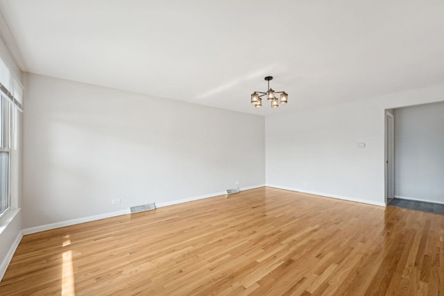 spare room with an inviting chandelier and light hardwood / wood-style floors