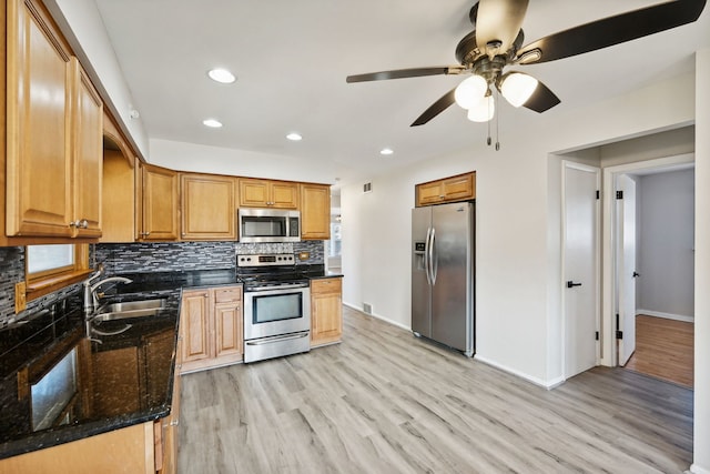 kitchen featuring ceiling fan, appliances with stainless steel finishes, dark stone counters, light hardwood / wood-style flooring, and sink