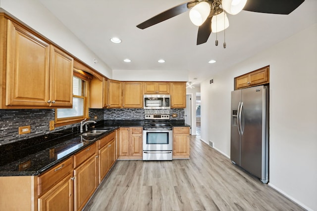 kitchen featuring ceiling fan, stainless steel appliances, light wood-type flooring, dark stone counters, and sink