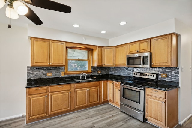 kitchen with ceiling fan, stainless steel appliances, light wood-type flooring, dark stone countertops, and sink