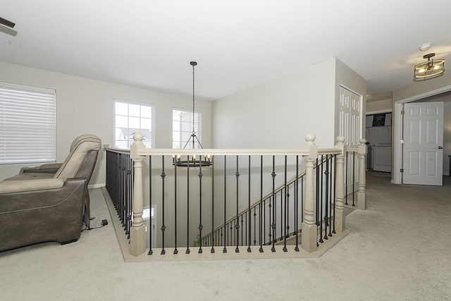 corridor with light carpet, washer / clothes dryer, and an inviting chandelier