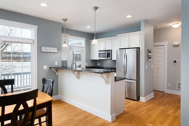 kitchen featuring white cabinetry, kitchen peninsula, a breakfast bar area, stainless steel appliances, and hanging light fixtures