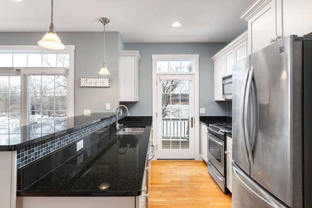 kitchen with appliances with stainless steel finishes, white cabinetry, sink, hanging light fixtures, and light hardwood / wood-style flooring