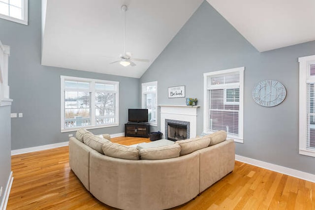 living room with light wood-type flooring, ceiling fan, a high end fireplace, and high vaulted ceiling