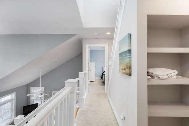 hallway featuring light colored carpet, built in shelves, and vaulted ceiling