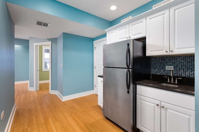 kitchen with white cabinets, decorative backsplash, stainless steel refrigerator, and sink