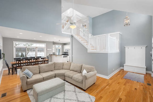 living room with ceiling fan, light hardwood / wood-style floors, and high vaulted ceiling