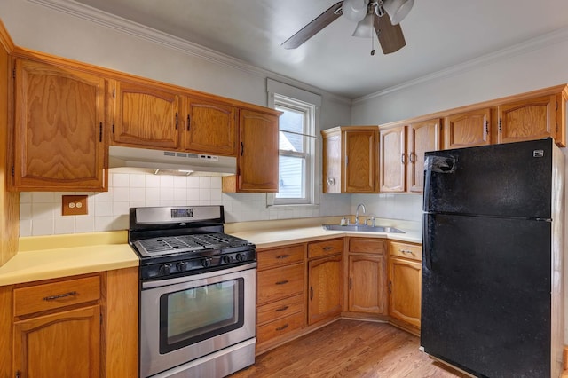 kitchen with sink, crown molding, light wood-type flooring, stainless steel gas range, and black refrigerator