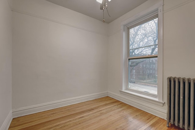 empty room featuring light wood-type flooring, a healthy amount of sunlight, and radiator heating unit