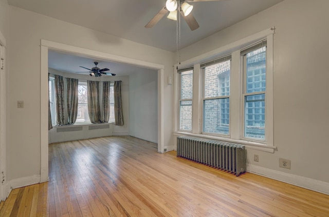 spare room featuring ceiling fan, light wood-type flooring, and radiator heating unit