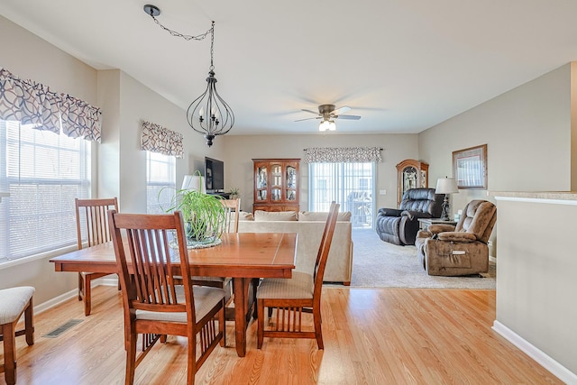 dining space featuring ceiling fan with notable chandelier, plenty of natural light, and light wood-type flooring