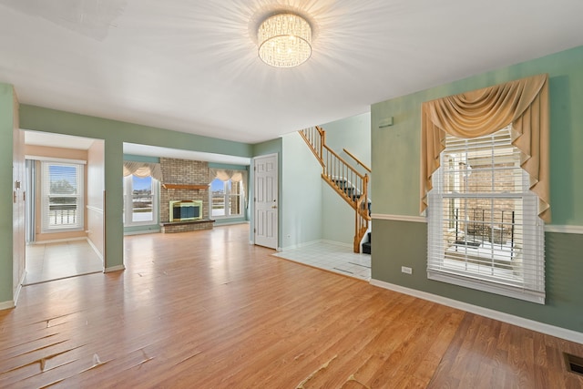 unfurnished living room with hardwood / wood-style flooring, a brick fireplace, and a chandelier