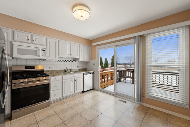 kitchen with appliances with stainless steel finishes, backsplash, light tile patterned flooring, stone countertops, and white cabinets