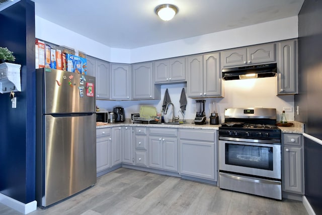 kitchen with stainless steel appliances, sink, gray cabinets, light wood-type flooring, and light stone counters